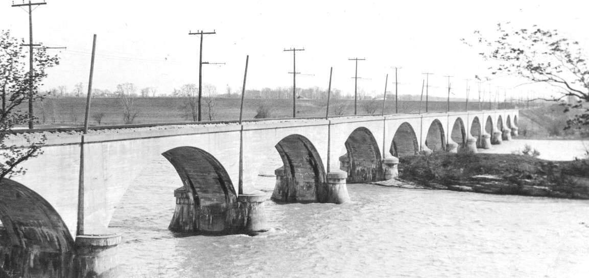 The Roche de Boeuf interurban bridge at Waterville, Ohio, photographed in 1921: a long line of concrete arches carrying a trolley line across the Maumee River. / El puente interurbano Roche de Boeuf en Waterville, Ohio, fotografiado en 1921: una larga hilera de arcos de hormig&oacute;n que cruza el r&iacute;o Maumee.