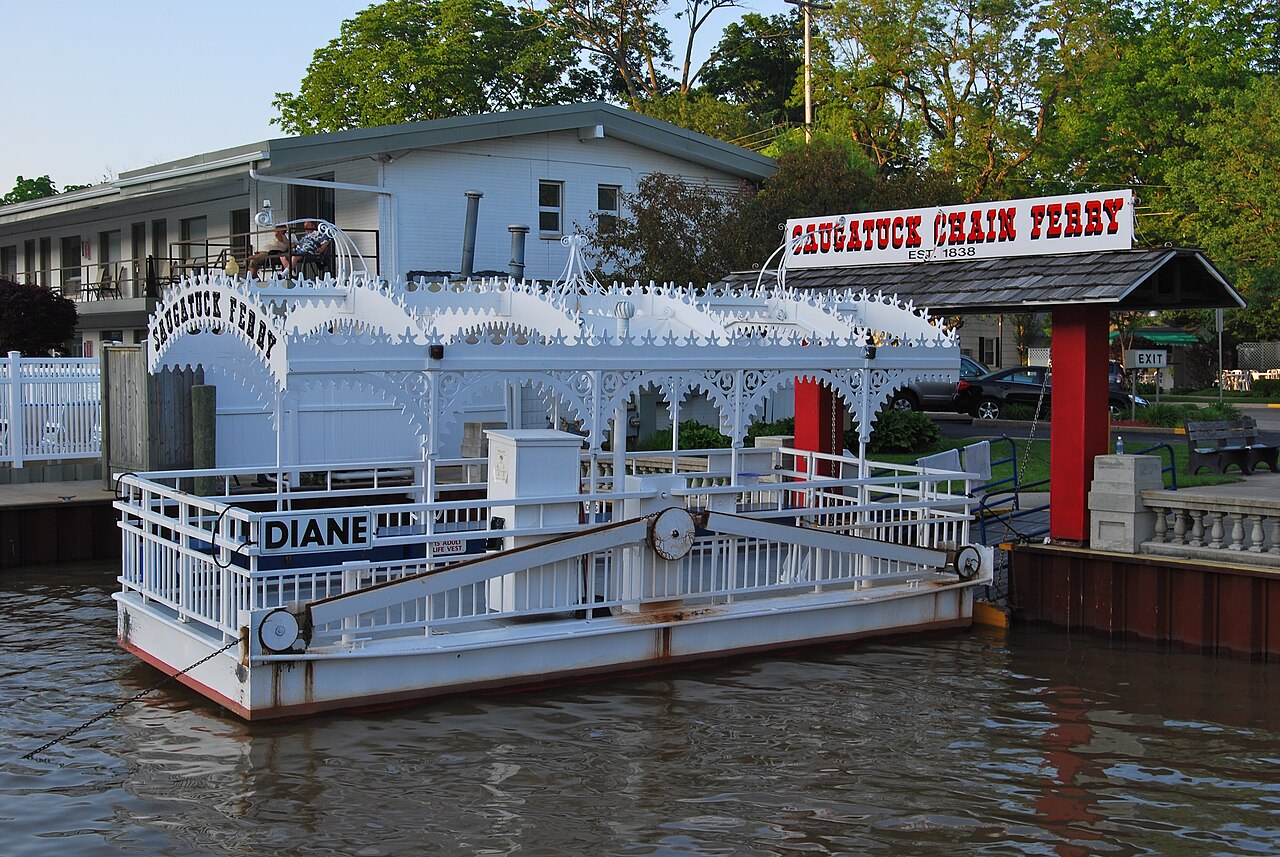 The Saugatuck chain ferry, a small flat open boat with a canopy, crossing the Kalamazoo River at Saugatuck, Michigan. / El transbordador de cadena de Saugatuck, una peque&ntilde;a barcaza abierta con toldo, cruzando el r&iacute;o Kalamazoo en Saugatuck, Michigan.