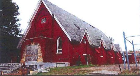A small red wooden church on Hamilton Street with a sagging roof and boarded entrance / Una pequeña iglesia roja de madera en Hamilton Street, con el techo vencido y la entrada tapiada