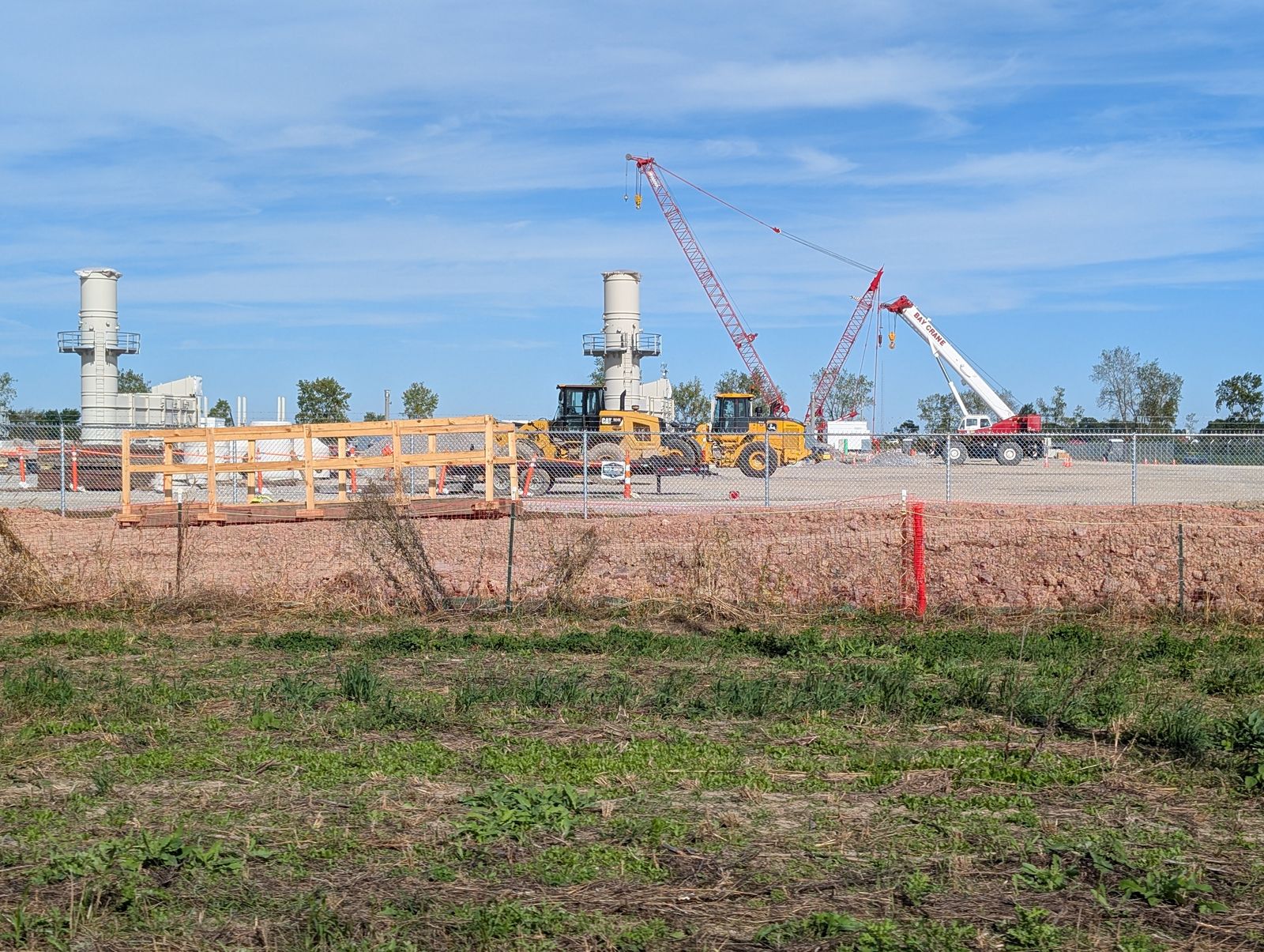Construction cranes, two tall exhaust stacks and earthmovers behind an orange fence at the corner of Mercer Road and Ohio 582 / Grúas de obra, dos altas chimeneas y maquinaria detrás de una valla naranja en la esquina de Mercer Road y la Ohio 582