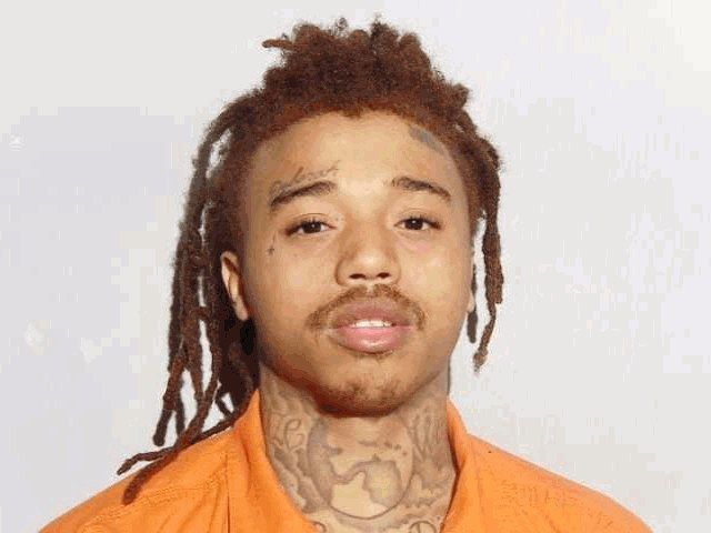 Booking photo of Jahiem D. Wright, a young man with long reddish locs and neck tattoos, in an orange jail uniform. / Foto de ingreso de Jahiem D. Wright, un joven con rastas largas rojizas y tatuajes en el cuello, con uniforme naranja de la cárcel.