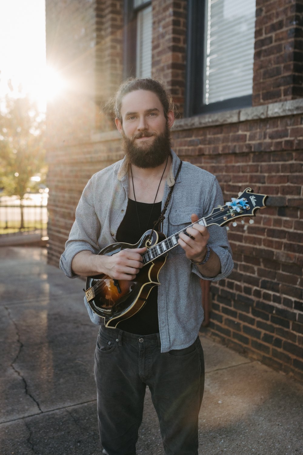 Gavin Gregg plays a mandolin beside a brick wall. / Gavin Gregg toca una mandolina junto a una pared de ladrillo.