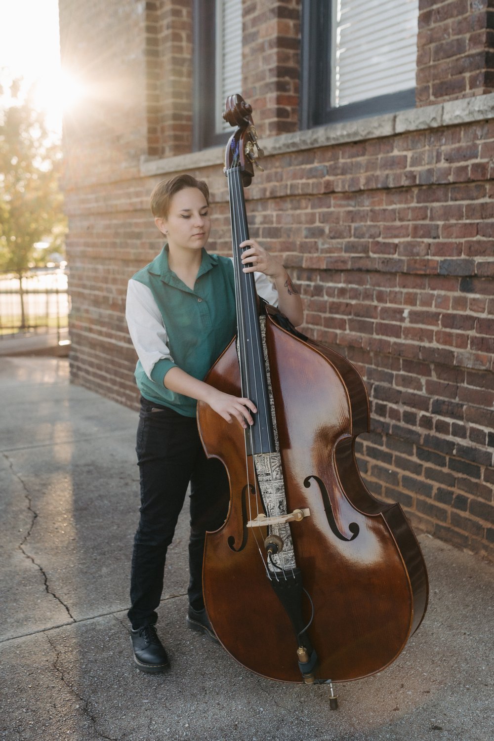 Katie Adams plays an upright bass beside a brick wall. / Katie Adams toca un contrabajo junto a una pared de ladrillo.