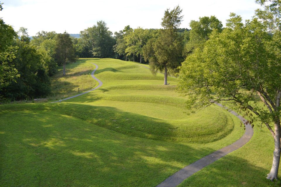 The same earthwork in low evening sunlight, the raised coils casting shadows that show their shape, with wooded hills beyond.